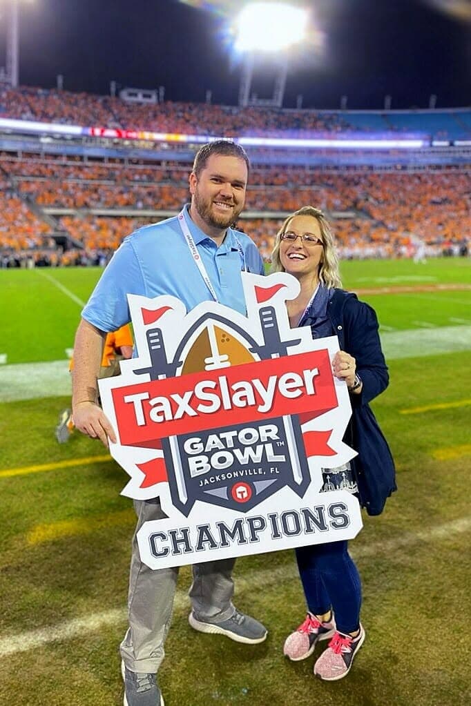Bret and his wife smiling together on the football field after the Gator Bowl, with the stadium crowd behind them