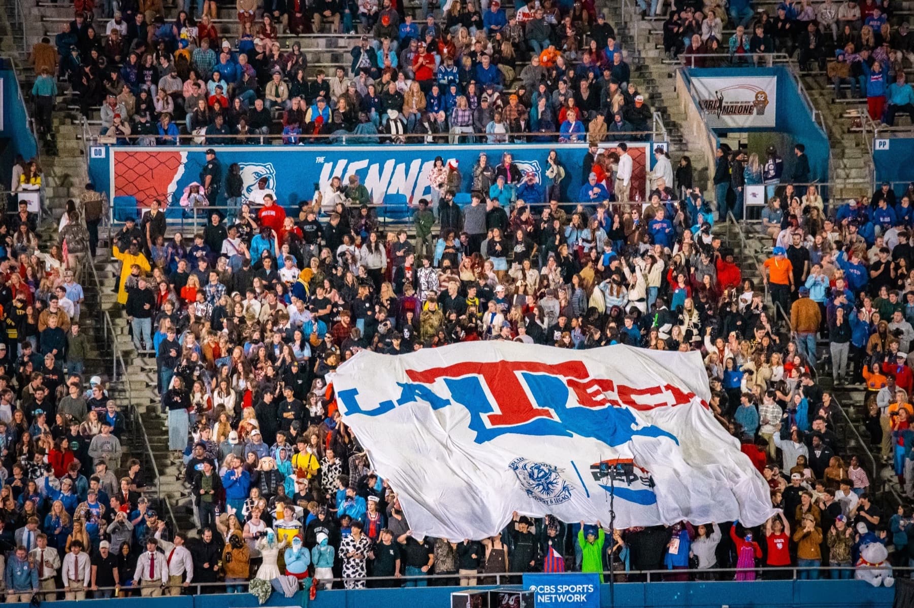 Louisiana Tech students gather around a large university flag in a crowded football section