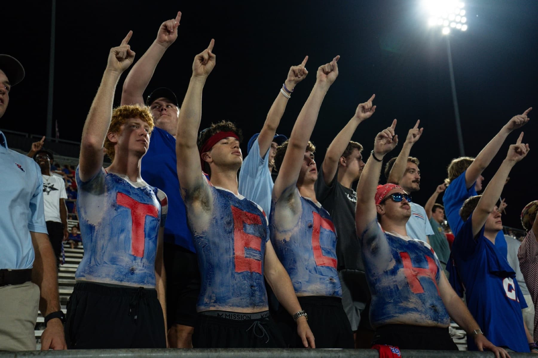 Four Louisiana Tech students with T E C H painted across their chests raise their arms with the crowd